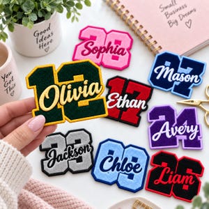 May include: A collection of varsity-style embroidered patches featuring various numbers and personalized names in different colors, including pink, dark green, navy blue, red, purple, silver, light blue, and black with contrasting borders.