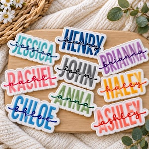 May include: A collection of nine rectangular name tags with scalloped edges, each featuring a name in bold block letters overlaid with the same name in a cursive script. The names include Jessica, Henry, Brianna, Rachel, John, Haley, Chloe, Anna, and Ashley in various colors.