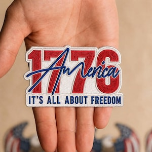 May include: A rectangular embroidered patch featuring the red numbers 1776 on a white background. The word America is stitched in blue script across the numbers. Below, the text IT'S ALL ABOUT FREEDOM is embroidered in blue capital letters.