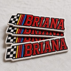 May include: Three embroidered patches stacked on top of each other. Each patch features the name "BRIANA" in red, outlined in black, with a white border. A checkered flag design and colorful stripes are on the left.