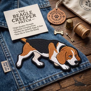 May include: An embroidered beagle patch in a creeping pose with black, brown, and white thread details. The patch is placed on blue denim fabric next to a product card labeled THE BEAGLE CREEPER PATCH, a leather tag, a thimble, and a spool of thread.