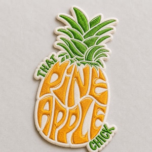 May include: Embroidered patch in the shape of a pineapple. The pineapple is yellow with green leaves and the words "THAT PINEAPPLE CHICK" in a stylized font.