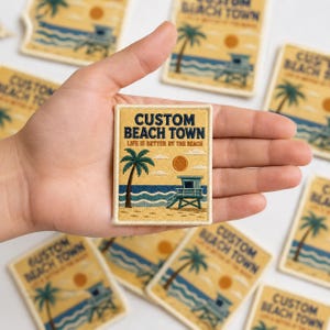 May include: A rectangular embroidered patch featuring a beach scene with a palm tree, a lifeguard tower, and a sun. The text reads CUSTOM BEACH TOWN and LIFE IS BETTER BY THE BEACH in dark blue and orange lettering against a yellow background.