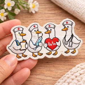 May include: Embroidered patch featuring four cartoon ducks dressed as medical professionals. Each duck wears a nurse's cap with a red cross. One duck holds a clipboard, another a syringe, a third a heart, and the last a stethoscope.