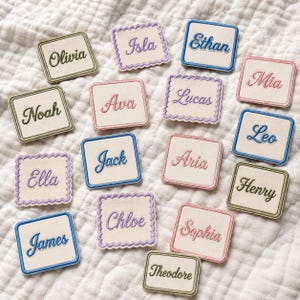 May include: A collection of square fabric patches featuring embroidered names including Olivia, Isla, Ethan, Noah, Ava, Lucas, Mia, Jack, Aria, Leo, Ella, Chloe, Sophia, James, and Theodore. The patches have either straight or scalloped edges.
