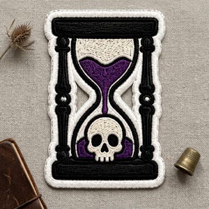 May include: An embroidered patch featuring a black hourglass frame with white borders. Inside, purple sand flows downward into a lower chamber containing a white human skull. The design is rendered in detailed thread work with black, white, and purple.