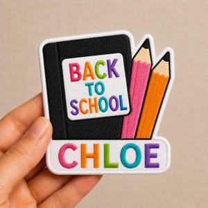 May include: Embroidered patch with a black notebook, pink and orange pencils, and the text "BACK TO SCHOOL" and "CHLOE" in colorful letters. The patch has a white border and is likely for a backpack or clothing.