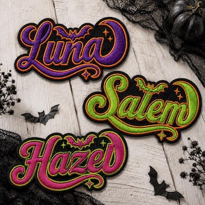 May include: Three embroidered patches with black backgrounds and orange borders. The top patch features the purple text Luna with a bat, the middle patch features the green text Salem with a bat, and the bottom patch features the pink text Hazel with a bat.