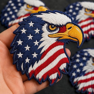 May include: An embroidered patch featuring the head of a bald eagle. The eagle's feathers are stylized with the American flag pattern, displaying a blue field with white stars on the left and red and white stripes on the right. The eagle has a yellow beak.