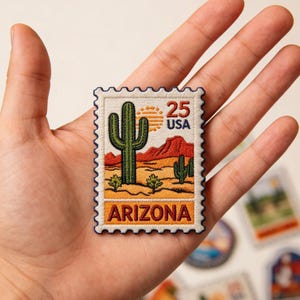 May include: Embroidered patch in the shape of a postage stamp featuring a desert landscape with a cactus, mountains, and the text "ARIZONA". The stamp also includes the text "25 USA". The patch has a white border.