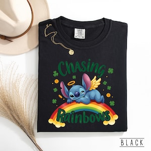 May include: Black sweatshirt with a cartoon character on a rainbow, text reading "Chasing Rainbows." The design includes shamrocks and gold coins. The word "BLACK" is at the bottom. A gold necklace and a hat are visible.