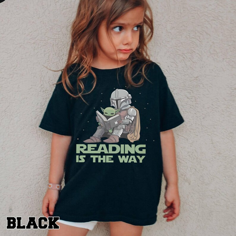 Puede incluir: Camiseta negra con un gr&aacute;fico de un personaje con armadura plateada leyendo un libro con un extraterrestre verde. El texto "READING IS THE WAY" est&aacute; debajo del gr&aacute;fico. La palabra "BLACK" est&aacute; en la parte inferior izquierda.