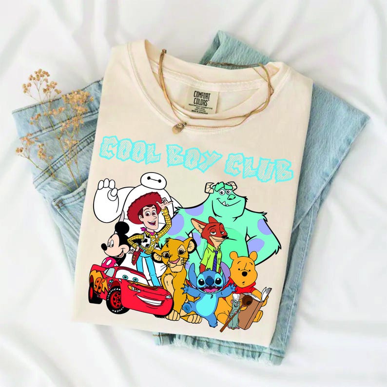 Może przedstawiać: Kremowy t-shirt z napisem COOL BOY CLUB jasnoniebieskimi literami nad grafiką przedstawiającą r&oacute;żne postacie animowane, w tym Myszkę Miki, Chudego, Zygzaka McQueena, Baymaxa, Simbę, Nicka Wilde'a, Sulleya, Sticha i Kubusia Puchatka.