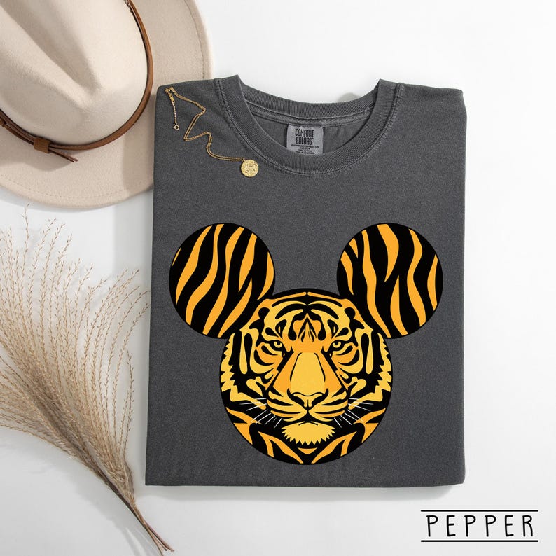 May include: Dark gray t-shirt featuring a tiger design with Mickey Mouse ears. The tiger's face is yellow and black, with black and yellow striped ears. The word "PEPPER" is printed at the bottom.