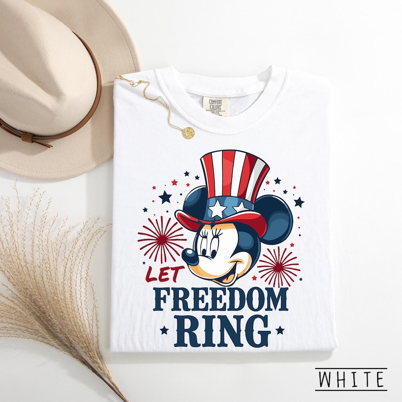 May include: White t-shirt featuring a patriotic Minnie Mouse design. Minnie Mouse is wearing a red, white, and blue Uncle Sam hat. The shirt has the text "LET FREEDOM RING" in navy blue with red star accents. The shirt is labeled "WHITE".
