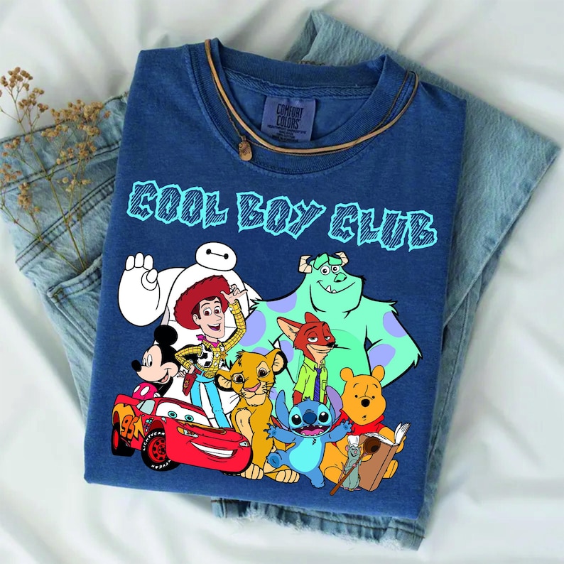 Może przedstawiać: Niebieski t-shirt z kr&oacute;tkim rękawem z napisem COOL BOY CLUB jasnoniebieskimi literami. Grafika przedstawia postacie Disneya: Baymaxa, Chudego, Myszkę Miki, Zygzaka McQueena, Simbę, Nicka Wilde'a, Sulleya, Sticha, Kubusia Puchatka i Remy'ego.