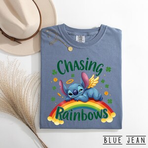 May include: Blue jean coloured t-shirt with the words "Chasing Rainbows" and a cartoon character lying on a rainbow. The shirt also features shamrocks and gold coins.