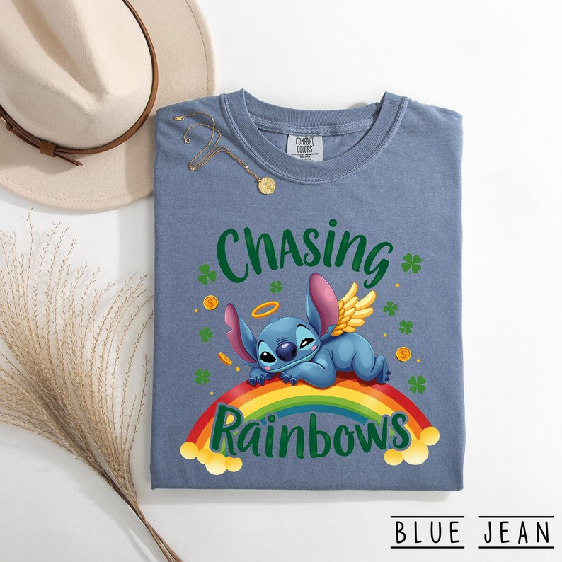 May include: Blue jean coloured t-shirt with the words "Chasing Rainbows" and a cartoon character lying on a rainbow. The shirt also features shamrocks and gold coins.