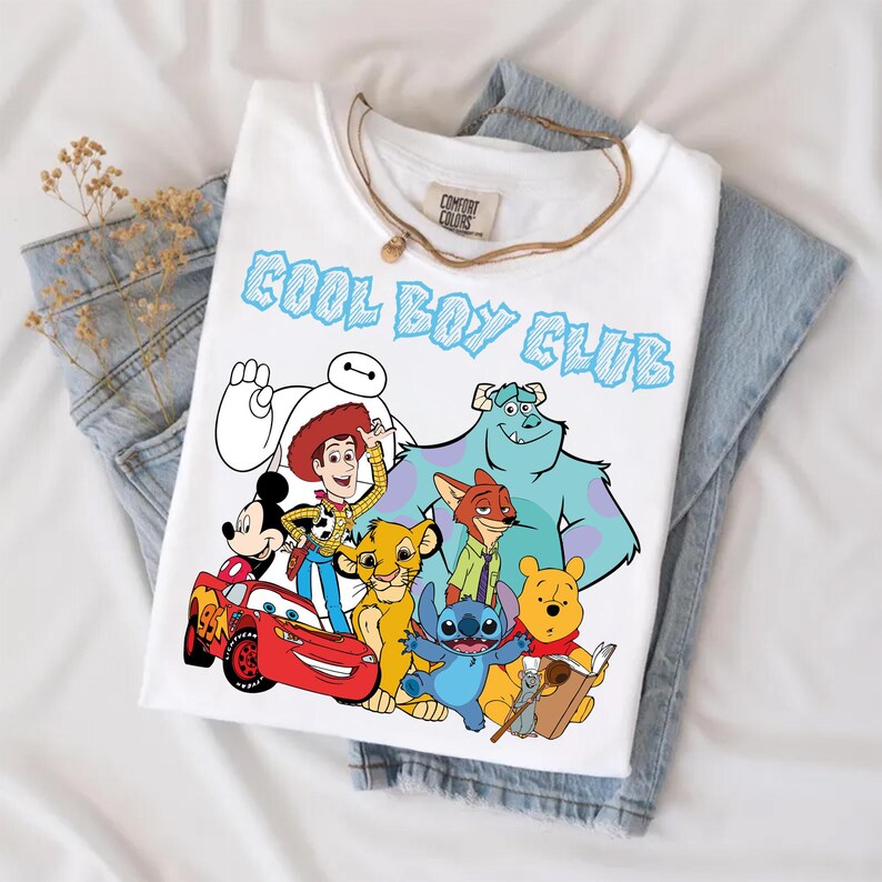 Może przedstawiać: Biały t-shirt z kr&oacute;tkim rękawem z napisem COOL BOY CLUB niebieskimi literami. Grafika przedstawia r&oacute;żne postacie animowane: Baymaxa, Chudego, Myszkę Miki, Zygzaka McQueena, Simbę, Nicka Bajera, Sulleya, Sticha, Kubusia Puchatka i Remy'ego.