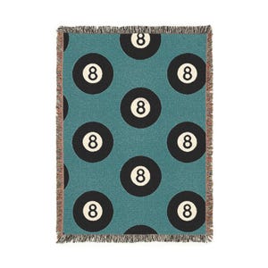 May include: Teal throw blanket with a repeating pattern of black eight balls. The blanket has a fringed edge in shades of brown and tan. The eight balls are black with white number 8s.