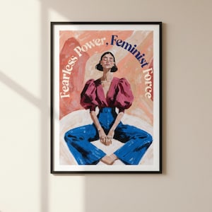 Può includere: Stampa artistica incorniciata con una figura seduta con un top rosa e pantaloni blu. L'opera d'arte presenta le parole "Fearless Power, Feminist Force" in un semicerchio. Lo sfondo è una miscela di toni rosa e pesca.
