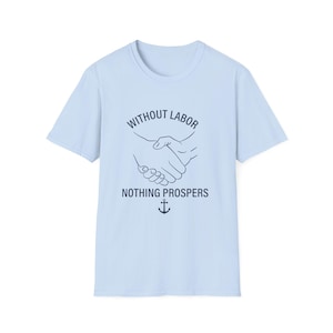 Può includere: Una t-shirt a maniche corte color azzurro con una grafica blu scuro che raffigura due mani che si stringono. Sopra la stretta di mano c'è il testo "WITHOUT LABOR" e sotto "NOTHING PROSPERS", seguito da una piccola icona di un'ancora.