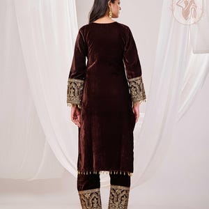 May include: A brown velvet two-piece outfit. The long-sleeved top and pants feature intricate gold embroidery on the cuffs and hems. The outfit is designed with a relaxed fit and is suitable for special occasions.