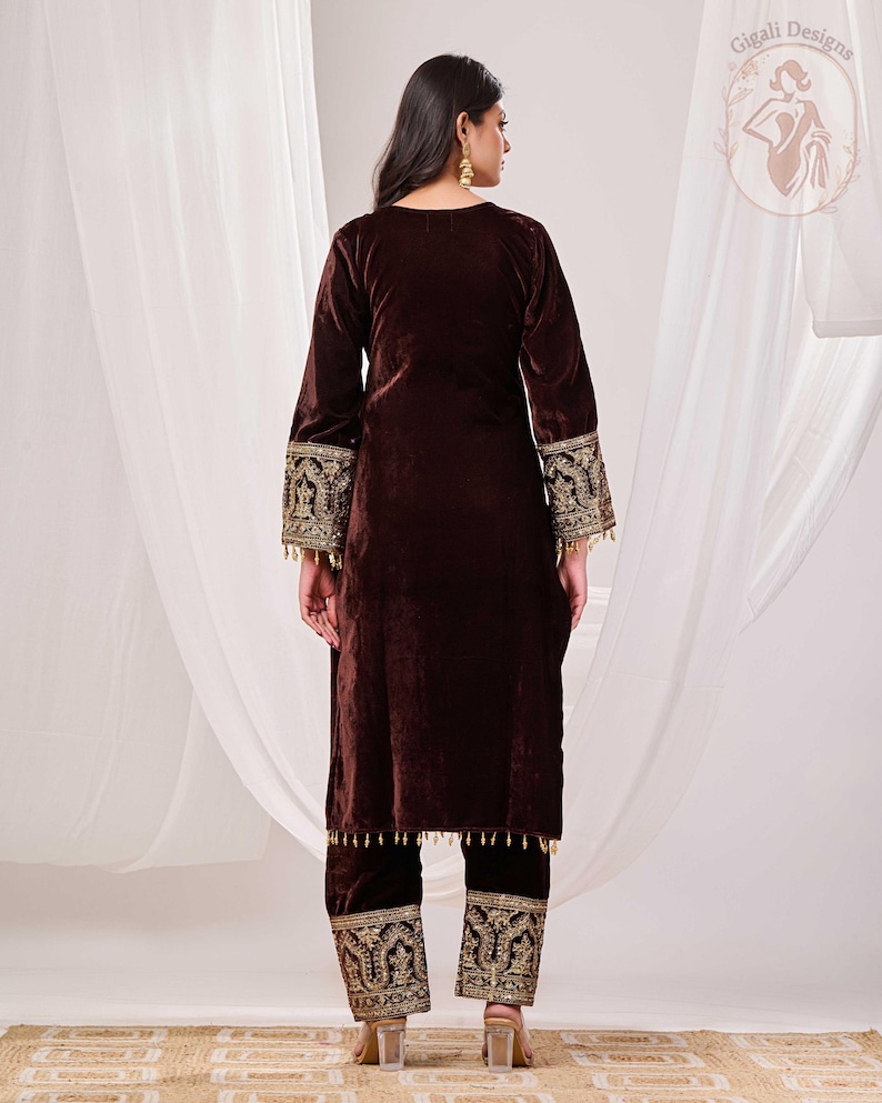 May include: A brown velvet two-piece outfit. The long-sleeved top and pants feature intricate gold embroidery on the cuffs and hems. The outfit is designed with a relaxed fit and is suitable for special occasions.