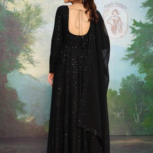 May include: A long black dress with long sleeves and a low back, decorated with sequins. A matching black shawl drapes over the shoulder. The dress is from the Gigali Designs collection.