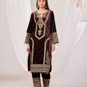 May include: A dark brown velvet outfit with intricate gold embroidery. The long-sleeved top features a keyhole neckline and ornate detailing around the collar, cuffs, and front panels. The matching pants have embroidered cuffs. The outfit is from Gigali Designs.