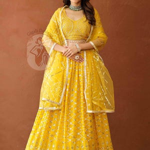 Puede incluir: Un vibrante conjunto lehenga amarillo. El conjunto incluye un top ajustado y adornado, una falda fluida y una dupatta transparente. Acentos plateados y detalles intrincados adornan el atuendo. El diseño general es elegante y festivo.