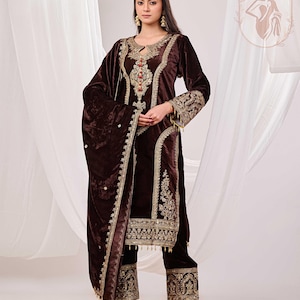 May include: A dark brown velvet salwar kameez with intricate gold embroidery. The ensemble includes a long-sleeved tunic, matching pants, and a shawl. The outfit features detailed embellishments around the neckline, cuffs, and hem.