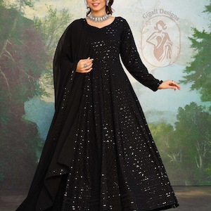 May include: A black, floor-length dress with long sleeves and a matching shawl. The dress is adorned with sequins and has a V-neck. The image also shows a silver necklace and earrings. The background features a painted landscape.