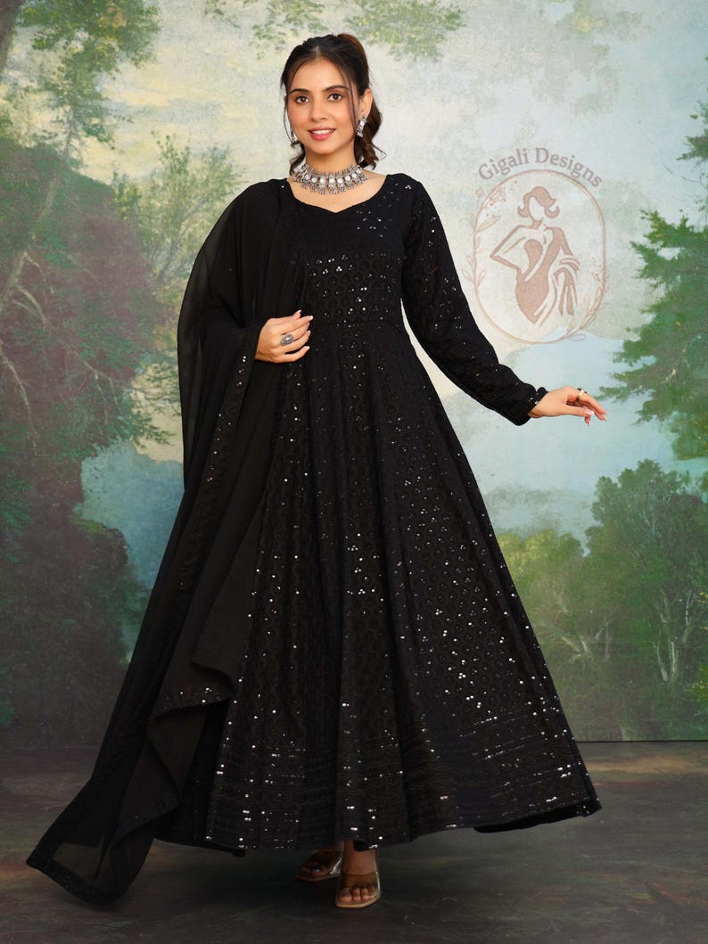 May include: A black, floor-length dress with long sleeves and a matching shawl. The dress is adorned with sequins and has a V-neck. The image also shows a silver necklace and earrings. The background features a painted landscape.