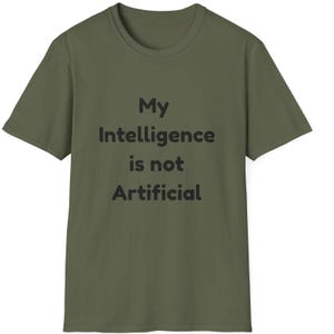 Könnte beinhalten: Olivgrünes T-Shirt mit dem schwarzen Text "My Intelligence is not Artificial". Das T-Shirt hat kurze Ärmel und einen Rundhalsausschnitt. Der Text ist mittig auf der Vorderseite platziert.
