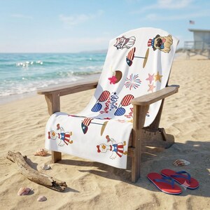 May include: A white beach towel draped over a wooden chair, featuring a repeating pattern of patriotic icons including a pug in a top hat, a goose in a dress, sunglasses, fireworks, starfish, and a coconut drink with the text America y'all.