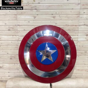 May include: A red, silver, and blue shield featuring a star emblem. The shield has a circular design with a red outer ring, a silver middle ring, and a blue centre with a silver star. The BlacksmithsTable logo is in the upper left corner.