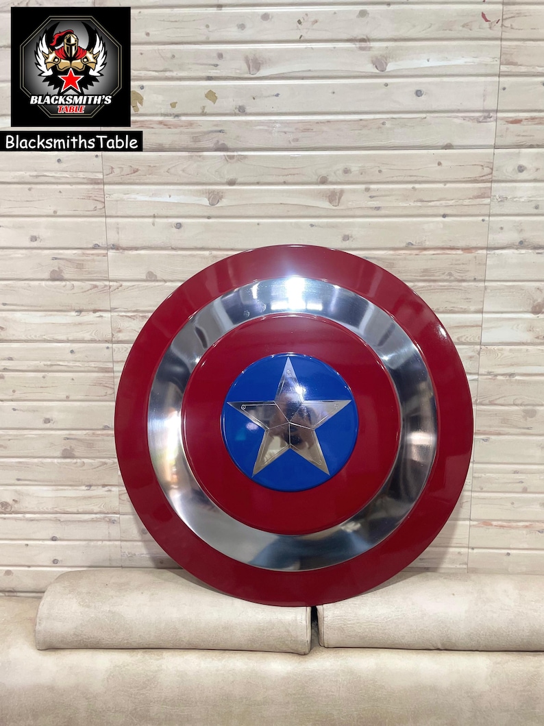 May include: A red, silver, and blue shield featuring a star emblem. The shield has a circular design with a red outer ring, a silver middle ring, and a blue centre with a silver star. The BlacksmithsTable logo is in the upper left corner.