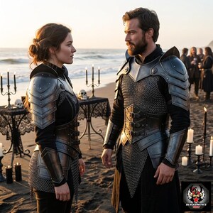 May include: Two people wearing medieval-style armor stand on a beach. The armor is silver and black, with chainmail and layered plates. The background includes a table with candles and skulls, and the ocean.