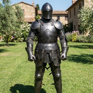 May include: A full suit of medieval armor, crafted in dark metal, stands on a grassy lawn. The armor includes a helmet, shoulder guards, chest and back plates, arm and leg protection, and gauntlets. The background features a stone building and trees.