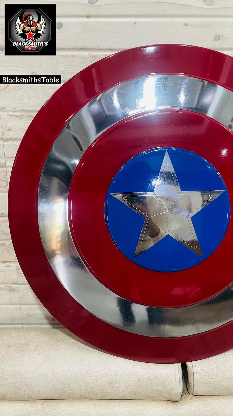 May include: A circular shield in red, silver, and blue, featuring a large silver star at its centre. The shield has a red outer ring, a silver middle ring, and a blue central disc. A replica of a superhero's shield.