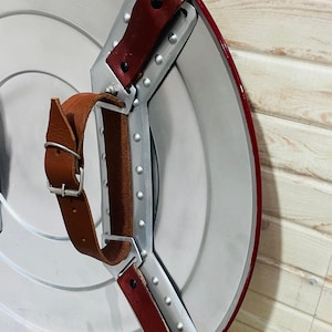 May include: A silver and red shield with brown leather straps and a metal handle. The shield has a red border and a silver centre. The text "Blacksmiths Table" is visible.