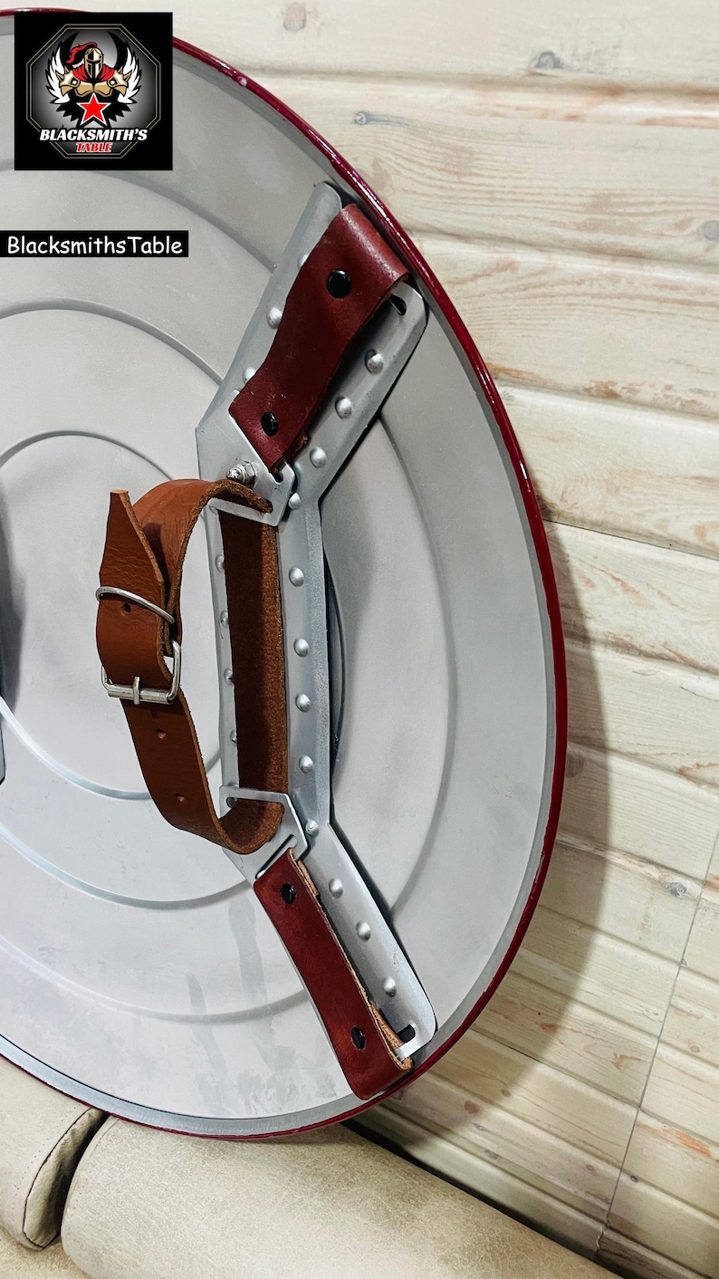 May include: A silver and red shield with brown leather straps and a metal handle. The shield has a red border and a silver centre. The text "Blacksmiths Table" is visible.