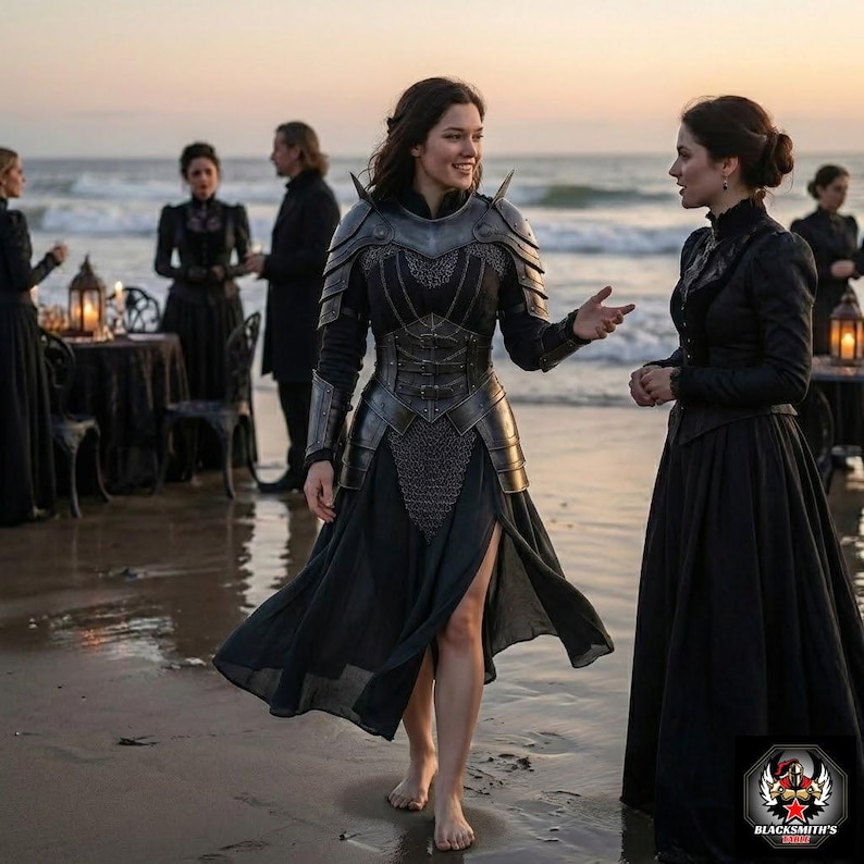 May include: A woman wearing a black dress with a metal breastplate and shoulder armor stands on a beach, conversing with another woman in a black dress. The scene is set at dusk, with the ocean in the background. Other people in black attire are visible.