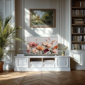 May include: A white entertainment center with a large flat-screen TV displaying a floral painting in shades of pink, orange, and red. A framed landscape painting hangs above the TV. A potted plant and a bookcase are also visible.