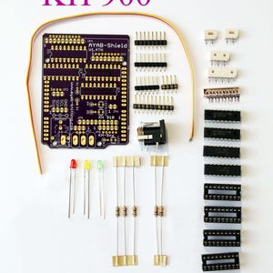 May include: A purple circuit board with the text "AYAB-Shield V1.4TH" and "KH 900" printed on it. The board is surrounded by various electronic components, including LEDs, resistors, and IC chips.