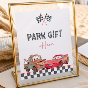 Puede incluir: Un letrero enmarcado con el texto "PARK GIFT Here" e ilustraciones de dos coches de carreras y banderas a cuadros. El letrero está en un marco dorado, perfecto para una fiesta o evento.
