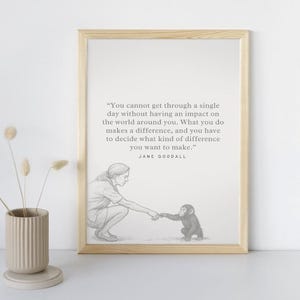 May include: A framed print with a light wood frame. The print features a pencil sketch of Jane Goodall and a chimpanzee, with a quote by Jane Goodall: "You cannot get through a single day without having an impact..."