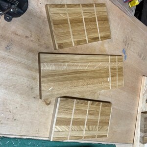 May include: Three unfinished wooden cutting boards with a light brown color and a rectangular shape. The boards are made of multiple wood pieces joined together. The boards are on a light brown wooden surface.