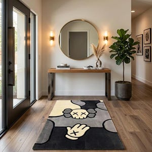 K&ouml;nnte beinhalten: Ein rechteckiger Teppich mit einem stilisierten Grafikdesign in einer Farbpalette aus Creme, Grau und Schwarz. Das Muster zeigt ein zentrales Totenkopfmotiv mit X-f&ouml;rmigen Augen und ein Handsymbol mit einem X auf der Handfl&auml;che in kr&auml;ftigen Linien.